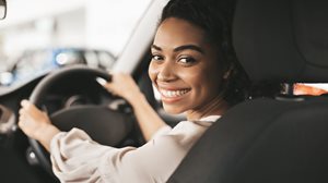 A happy young woman drives away after getting a great deal on a new car.