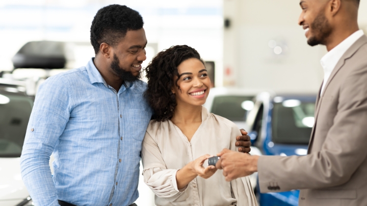 A happy couple grabbing car keys from a dealer after they purchased a car.